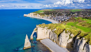 Aerial view of a coastal landscape featuring dramatic cliffs, a sandy beach, and a small town near the shoreline, showcasing the beauty of nature and the sea.